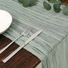 A silver fork and knife rest on a light green cotton gauze table runner on a dark wooden table.