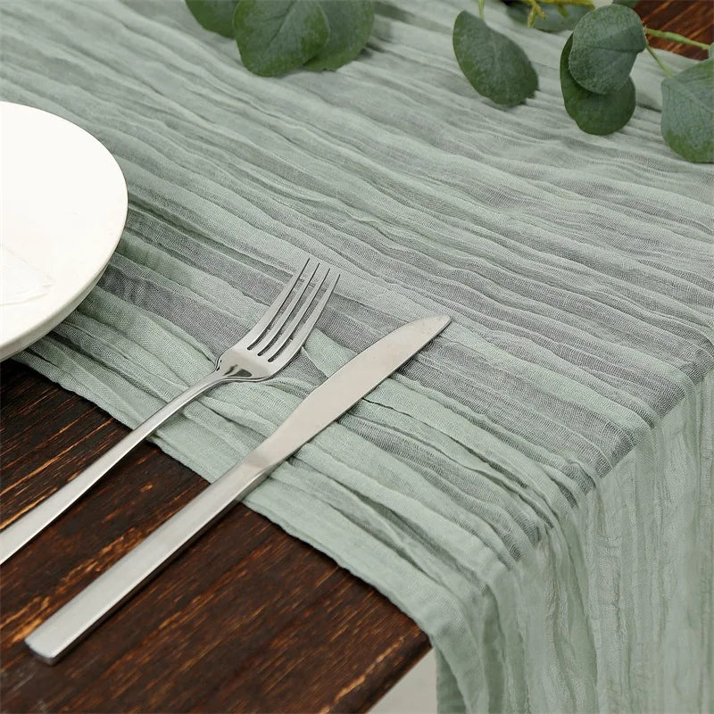 A silver fork and knife rest on a light green cotton gauze table runner on a dark wooden table.