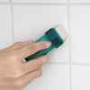 A hand holds a green reusable limescale and stain eraser tool against a white tiled surface.