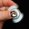 A hand is holding a silver fidget spinner with a translucent amber gemstone on the top.