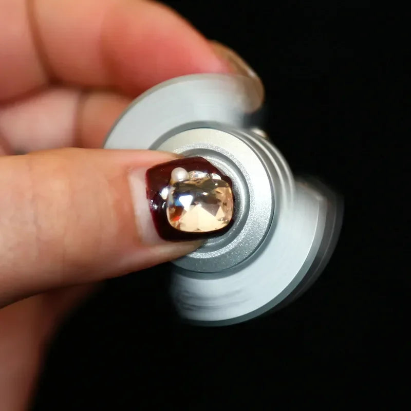 A hand is holding a silver fidget spinner with a translucent amber gemstone on the top.