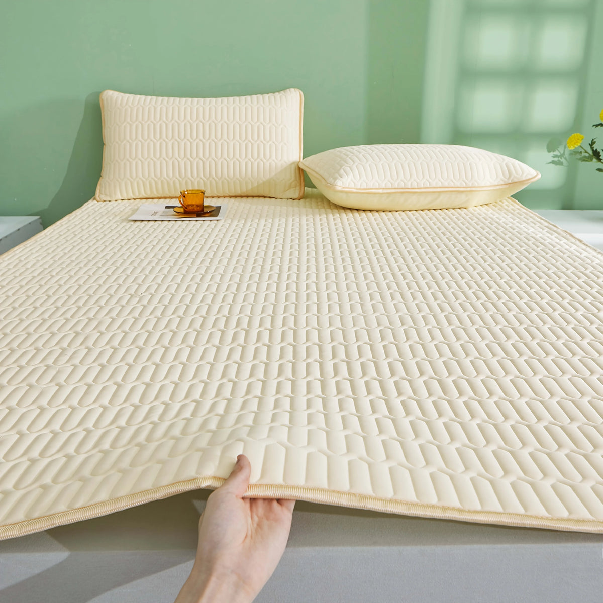 Primer plano de una almohada enfriadora beige transpirable con textura acolchada y dos almohadas sobre una superficie verde c