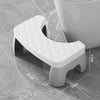 A white ergonomic non-slip toilet squat stool with a diamond pattern, shown on a gray tiled floor.