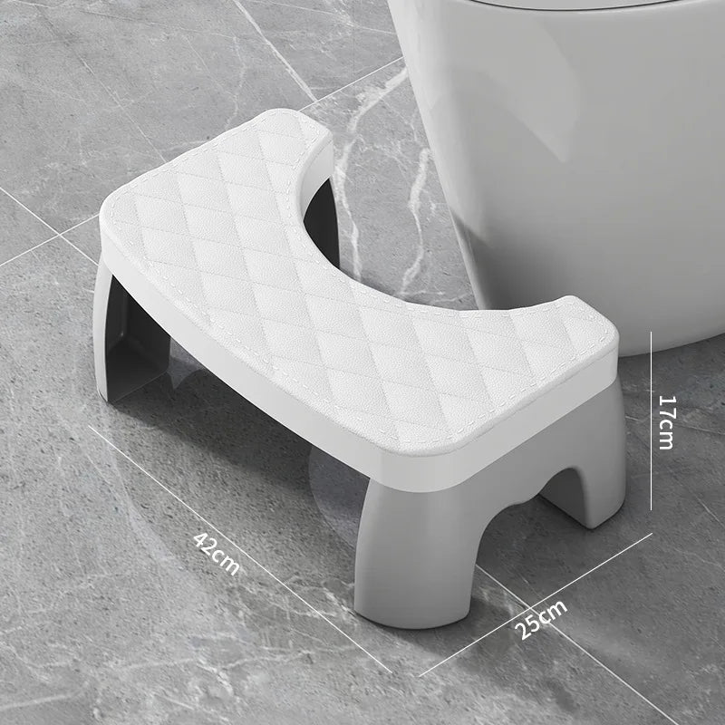 A white ergonomic non-slip toilet squat stool with a diamond pattern, shown on a gray tiled floor.