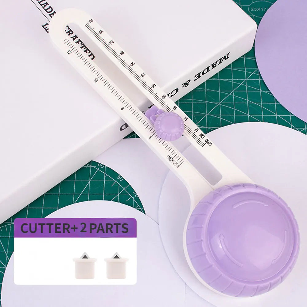 A white adjustable circular paper cutter with a purple blade and two interchangeable parts resting on a green cutting mat.