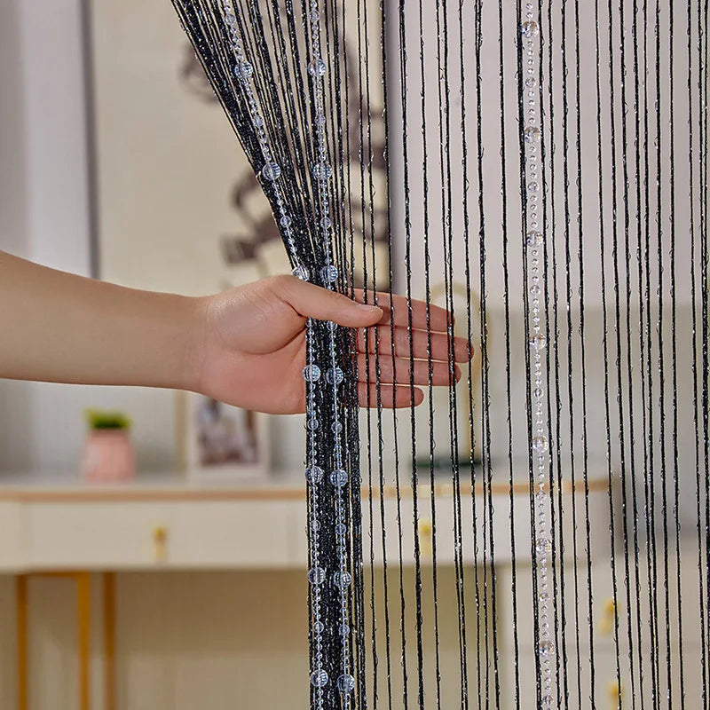 A hand is adjusting a sheer black and clear crystal beaded string curtain for a doorway or window.
