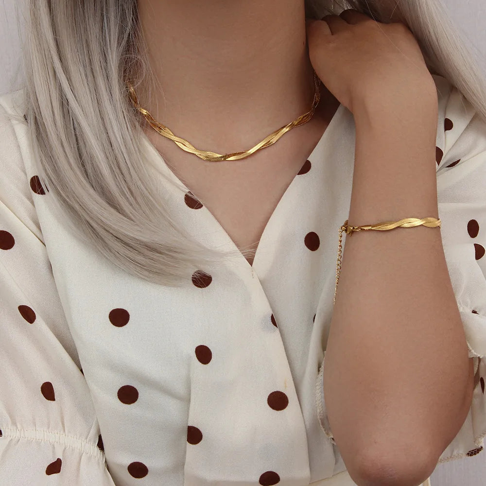 A close-up of a woman wearing a gold-plated herringbone chain necklace and bracelet set with a polka dot blouse.