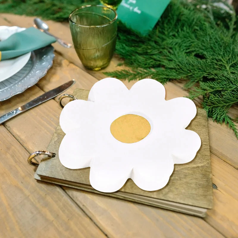 A white daisy flower cutout rests on a brown card next to a green pine branch and silverware.