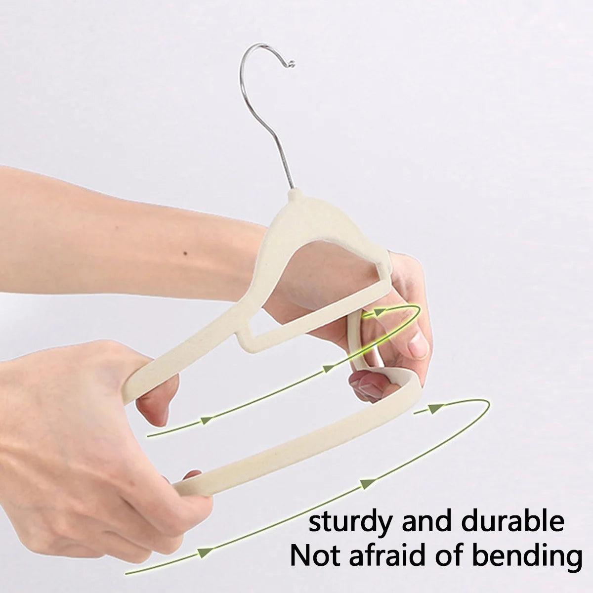 Hands holding a light beige velvet hanger with a wire hook, demonstrating its sturdy and durable bending capability.