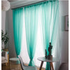Light aqua sheer voile curtains hanging in a window with decorative greenery and a small table.