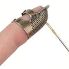 A vintage metal sewing thimble with a finger protector ring is shown on a hand.
