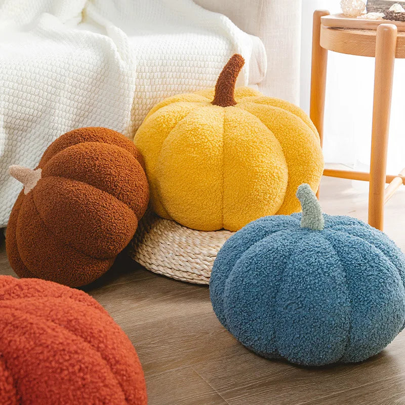 A collection of soft, fuzzy Halloween pumpkin plush pillows in orange, yellow, and blue resting on a wooden floor.