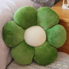 A plush sunflower pillow with green petals and a cream center, resting on a light fabric surface.