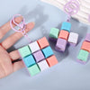 A hand holds a colorful tactile clicking keyboard keychain fidget toy with pink and purple components.