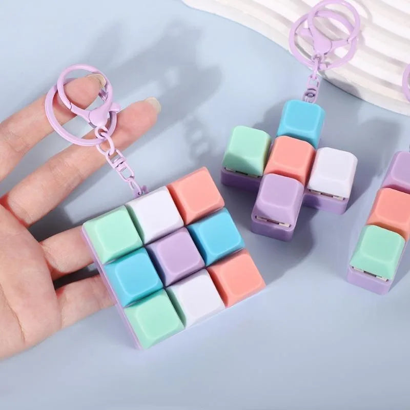 A hand holds a colorful tactile clicking keyboard keychain fidget toy with pink and purple components.