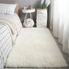 A fluffy white silk-touch area rug placed in a bright room with a plant and decorative items.