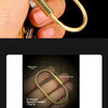 A hand holds a brass gold U-shaped keychain charm with a secure carabiner clip.