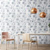 A modern dining room wall featuring a gray and white botanical leaf wallpaper with round gold decorative objects.