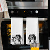 A set of two white kitchen towels featuring illustrations of dogs with glasses and a glass of wine.