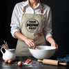 A person wearing a beige canvas apron with a circular design is shown next to kitchen tools and ingredients.