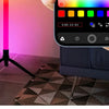 A hand holds an RGB LED floor lamp, showing a color wheel interface on the device.