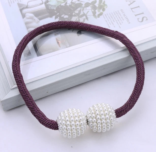 A purple cord bracelet with pearl magnetic curtain clips displayed on a white surface.