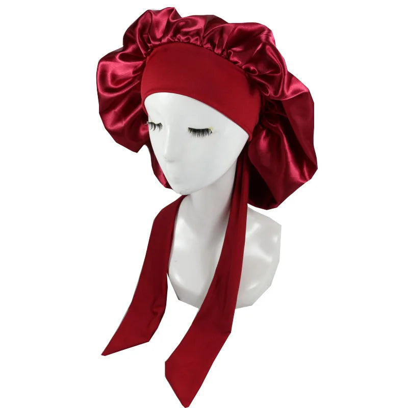 A deep red satin sleep cap with a ruffled crown and long ties displayed on a white mannequin head.