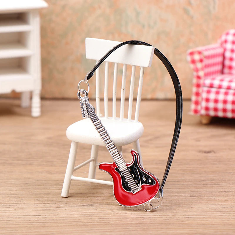 A black guitar-shaped necklace with a red body and silver accents displayed on a wooden surface.
