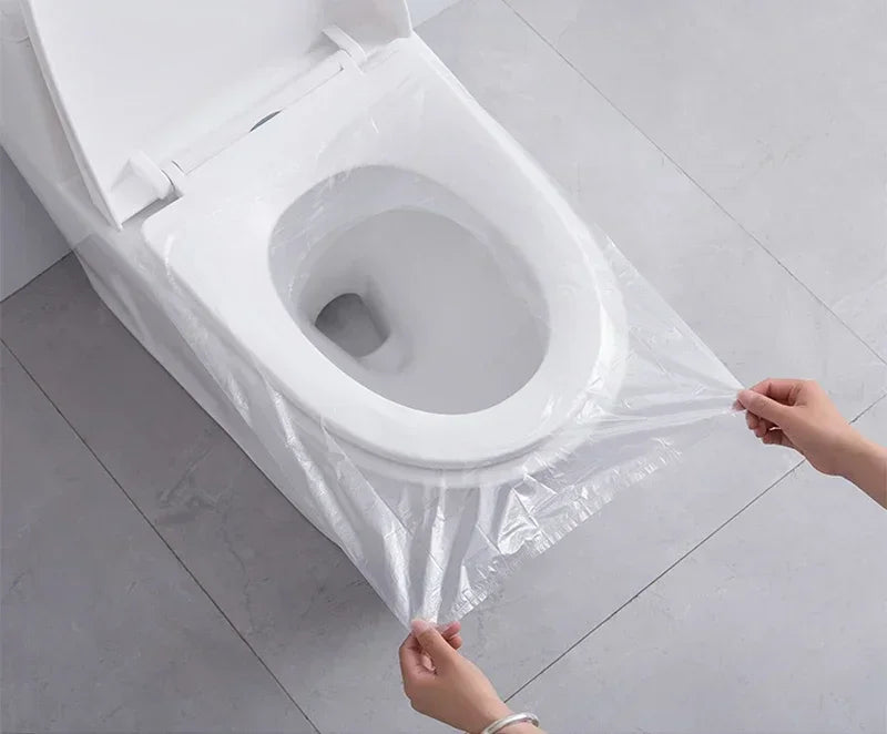 A hand is placing a plastic waterproof toilet seat cover over a white toilet bowl.