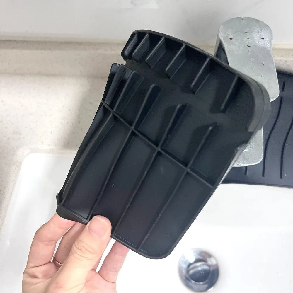 A hand holds a black silicone faucet splash mat designed to catch water on a countertop.