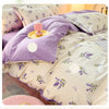 Lavendelförmige Bettdecke mit weißen Akzenten und einem rosa Zierkissen auf einem Bett.