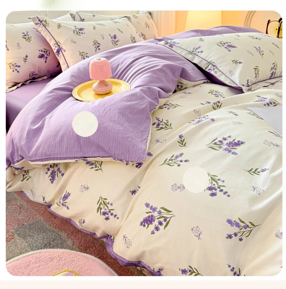Lavendelförmige Bettdecke mit weißen Akzenten und einem rosa Zierkissen auf einem Bett.