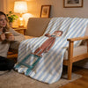 A person is sitting on a sofa with a striped blanket featuring a cartoon character.