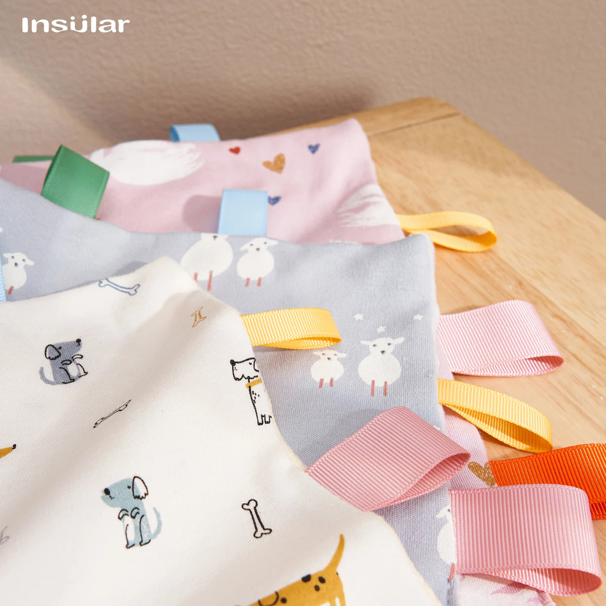 A close-up of a baby sensory tag comfort blanket with soothing teether in pink, blue, and yellow colors.