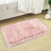 A fluffy pink silk-touch area rug placed on a light wooden floor next to a white sofa.