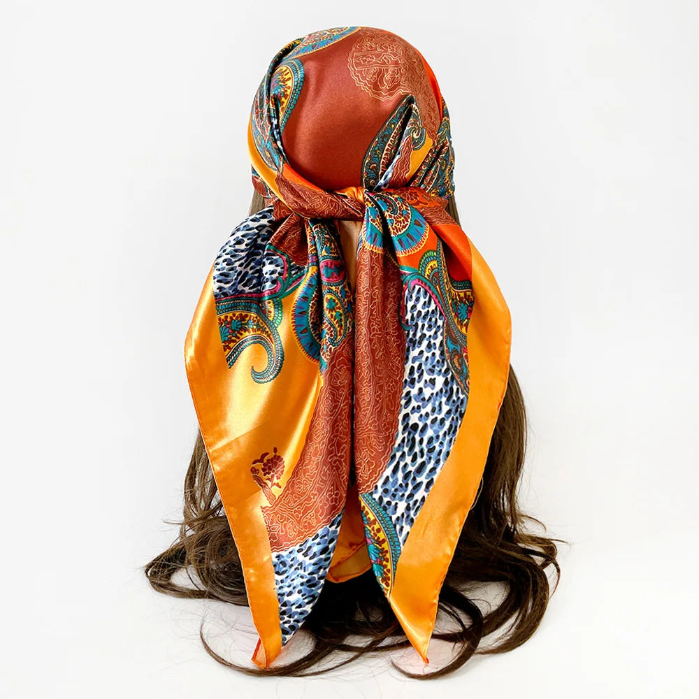 A vibrant orange and blue leopard paisley square scarf tied around a dark hair