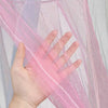 A hand is holding and displaying a sheer pink mosquito net fabric with purple tint.