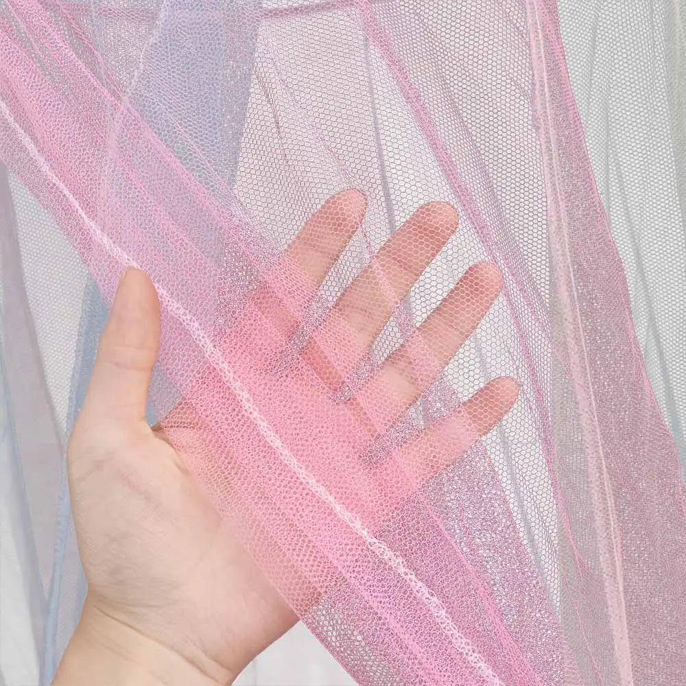 A hand is holding and displaying a sheer pink mosquito net fabric with purple tint.