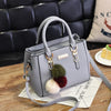 A light gray vintage PU leather shoulder bag with gold hardware and a tassel detail resting on a wooden surface.