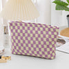 A purple and yellow plaid makeup bag with a zipper resting on a white surface next to a lamp and cosmetic items.