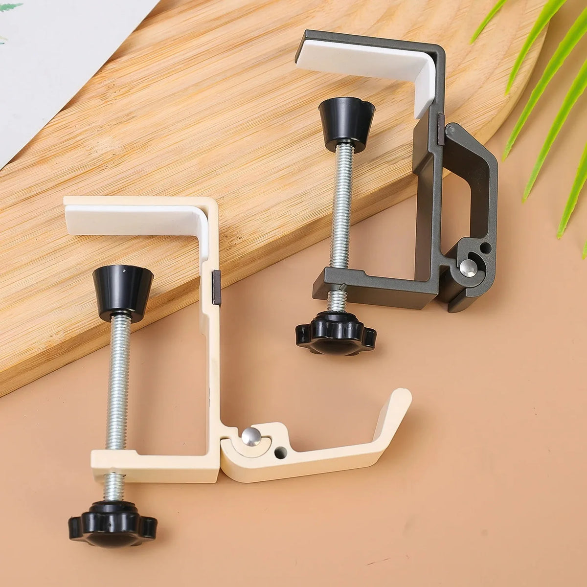 A set of foldable aluminum desk hooks with black grips and light wood accents shown on a wooden surface.
