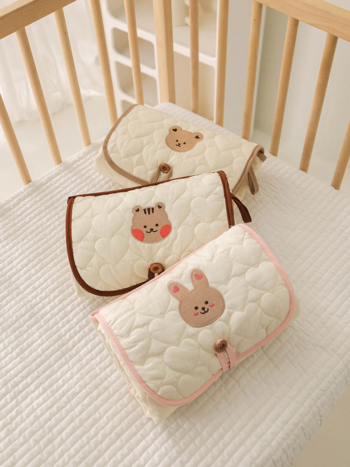 Three quilted beige and pink foldable portable diaper changing pads are displayed on a white surface.