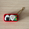 A red container holds a white cake-shaped fidget keychain with black icing and green decorations.