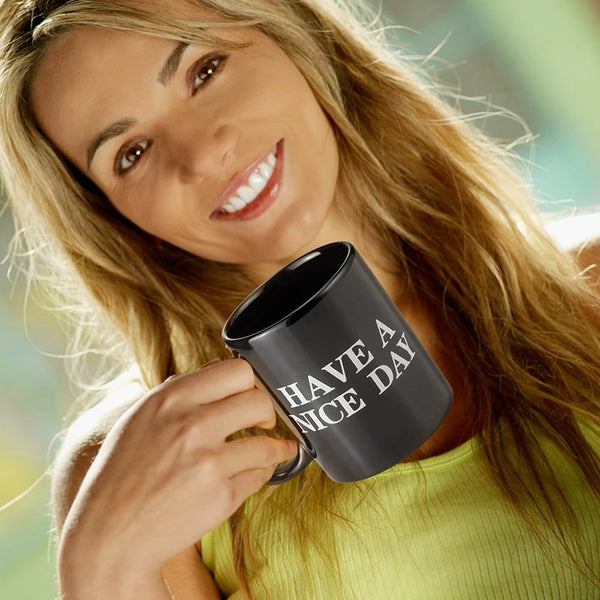 Une femme blonde tient une tasse à café noire avec l'inscription HAVE A NICE DAY.