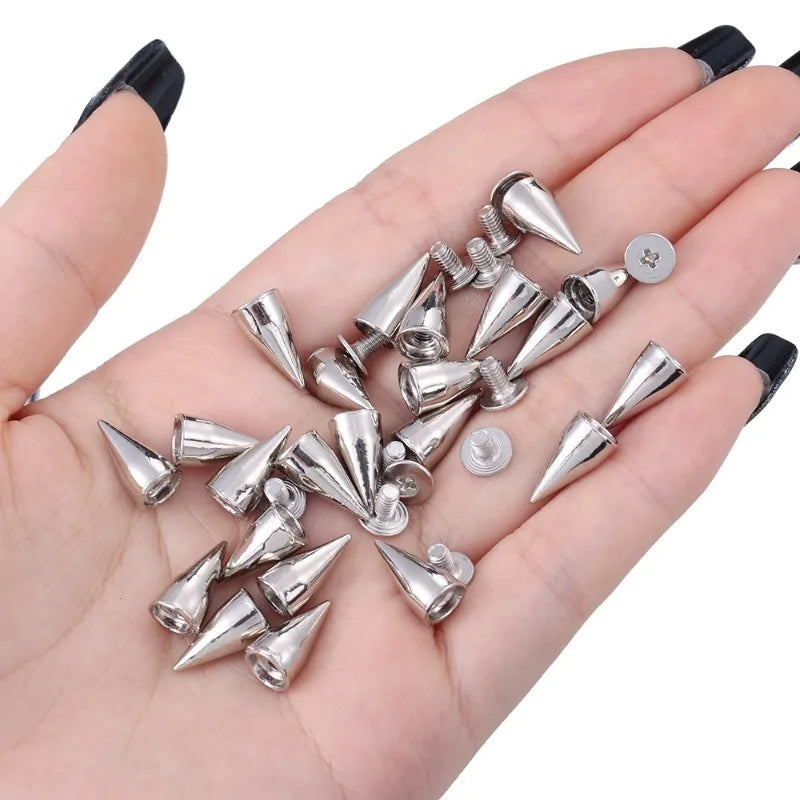 A hand holds a collection of silver metal spike studs for DIY clothing and accessories.
