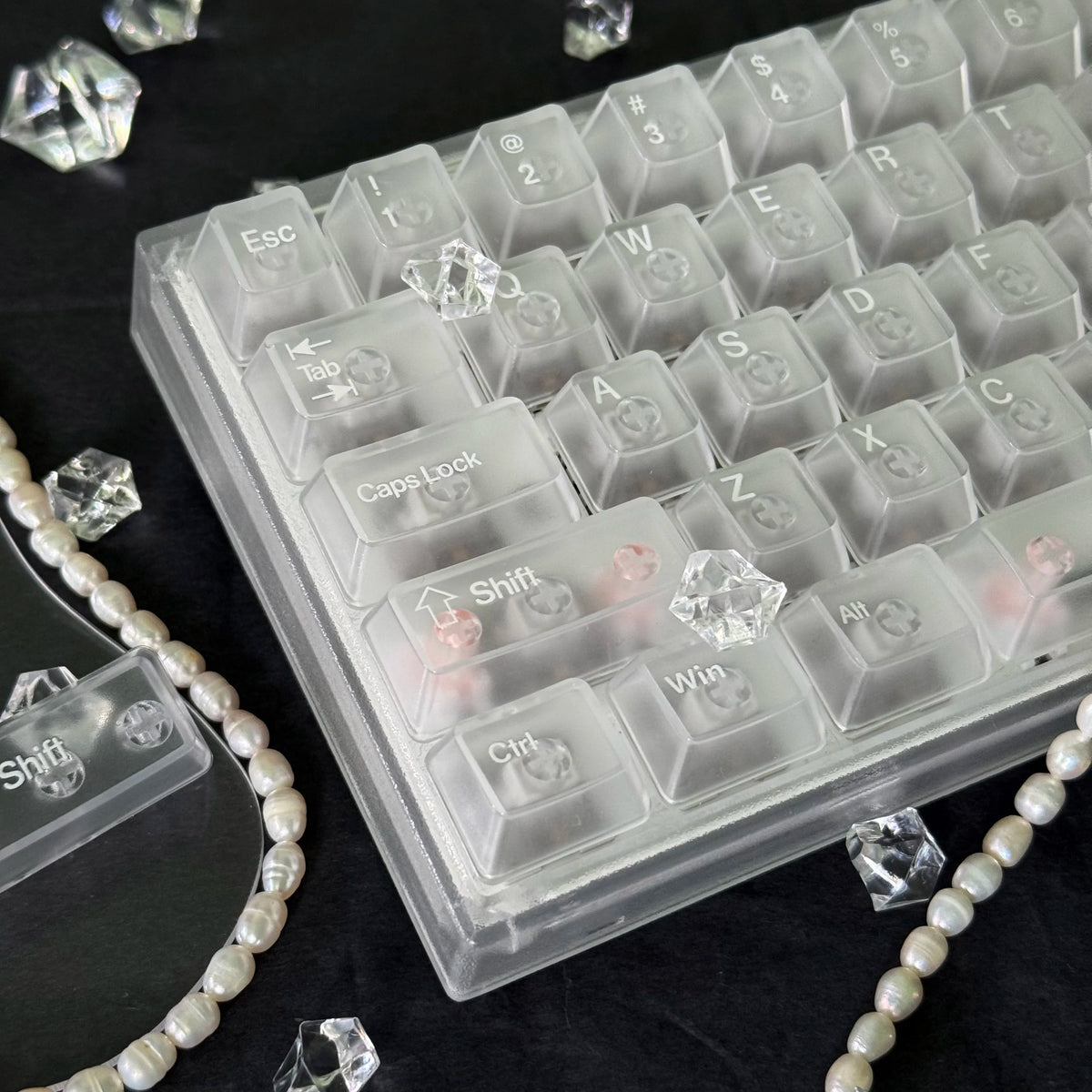 A close-up view of translucent PC keycaps for a mechanical keyboard, showing various keys and a pearl necklace.