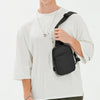 A male model wearing a white t-shirt and olive pants, holding a black convertible sling bag.