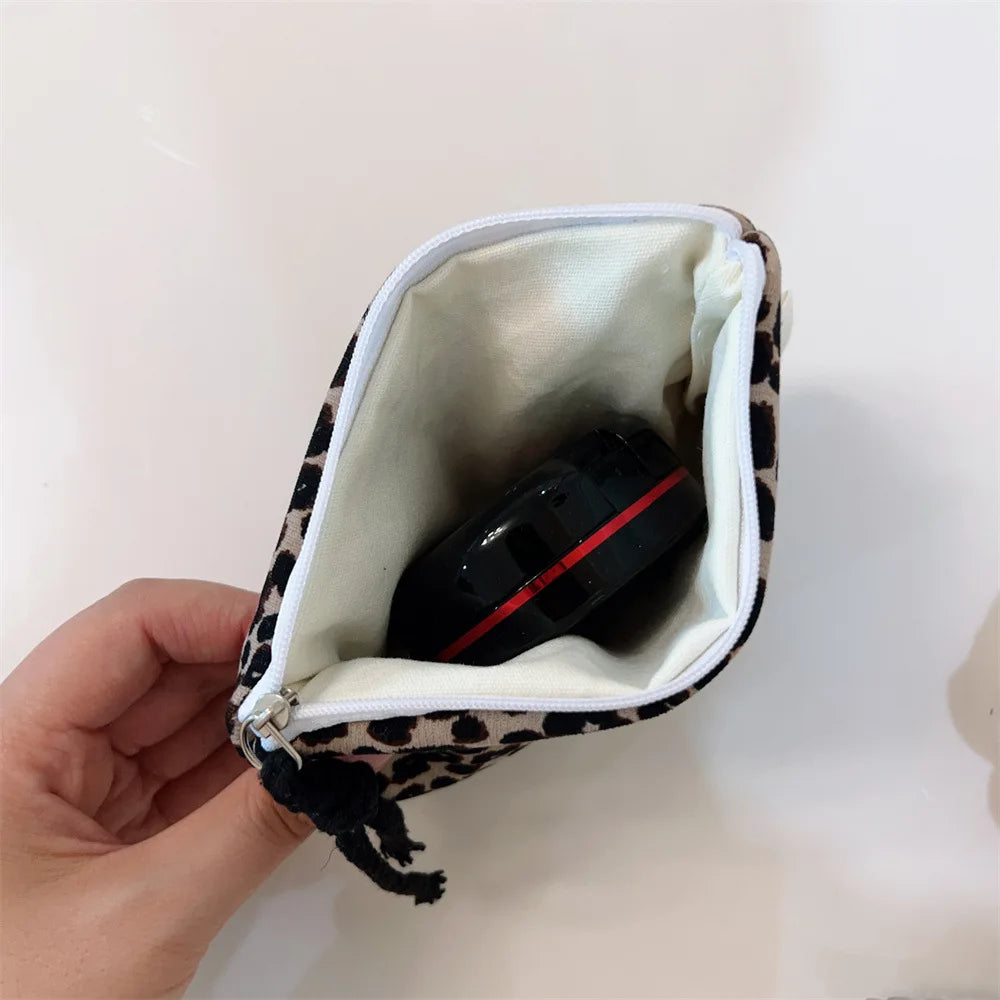 A hand holds an open leopard print cosmetic bag with a secure zipper, revealing a black item inside.