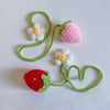 Handmade crochet strawberry with a flower and green stem, used as a mirror pendant.