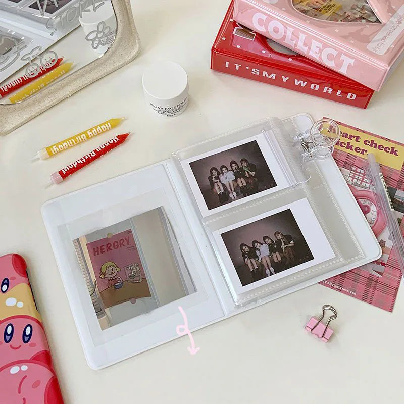 A white mini photo album with clear pockets is shown next to various collectible items and art supplies.